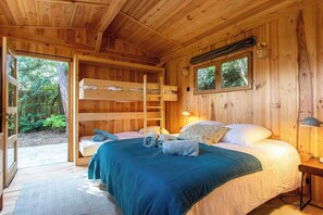 Une chambre dans un chalet en bois, avec un lit superposé, un lit simple et une fenêtre donnant sur une forêt.