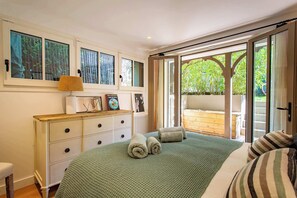 Quarto com cama, penteadeira, luminária e vista para um jardim pela porta de correr.
