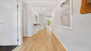 Un couloir avec un plancher en bois, des murs blancs et une porte sur le côté gauche.