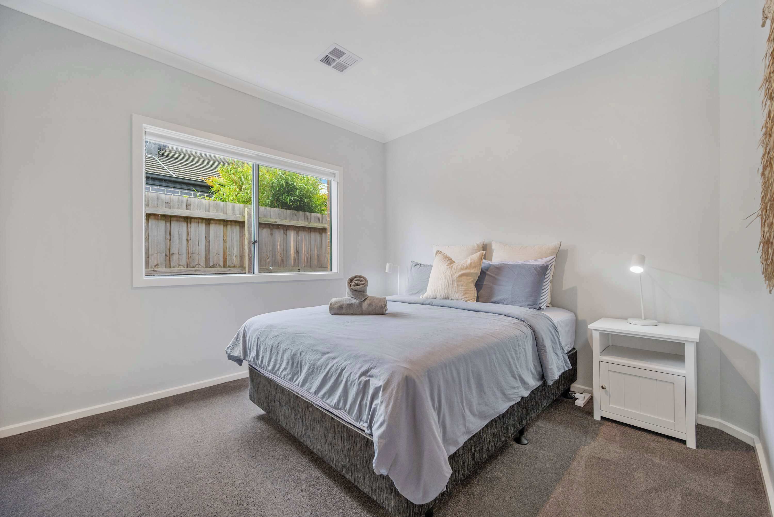 A bedroom with a bed, a nightstand, a window, and a view of the outside.