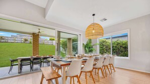 Un coin repas avec une grande table dressée pour six personnes, entourée de chaises, et un luminaire suspendu au-dessus.
