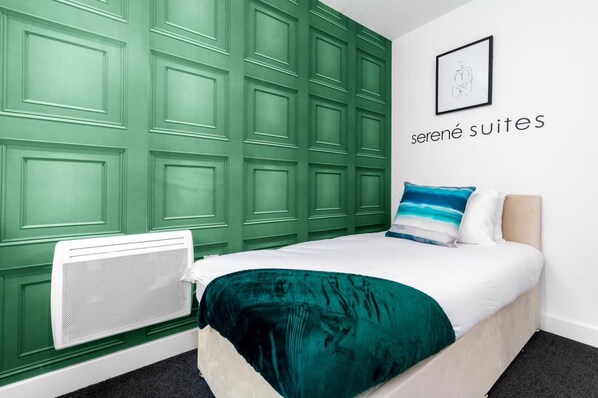 A bedroom with a green paneled wall, a bed with a teal blanket, and a white radiator.
