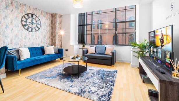 A modern living room with two sofas, a coffee table, a large wall clock, and a TV displaying a movie poster.