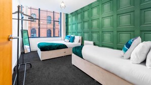 A hotel room with two beds, a large window with a view of a brick building, and a green wall paneling.