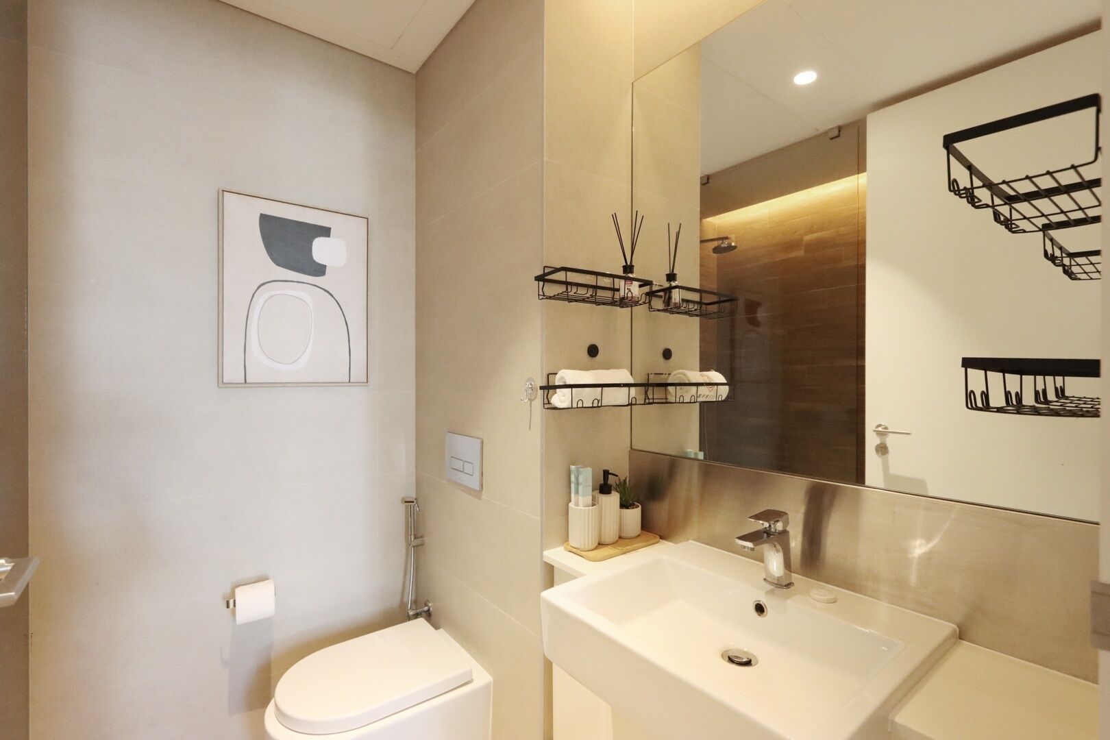 Uma casa de banho moderna com sanita, lavatório e espelho. Há prateleiras com artigos de higiene pessoal e um porta-toalhas.