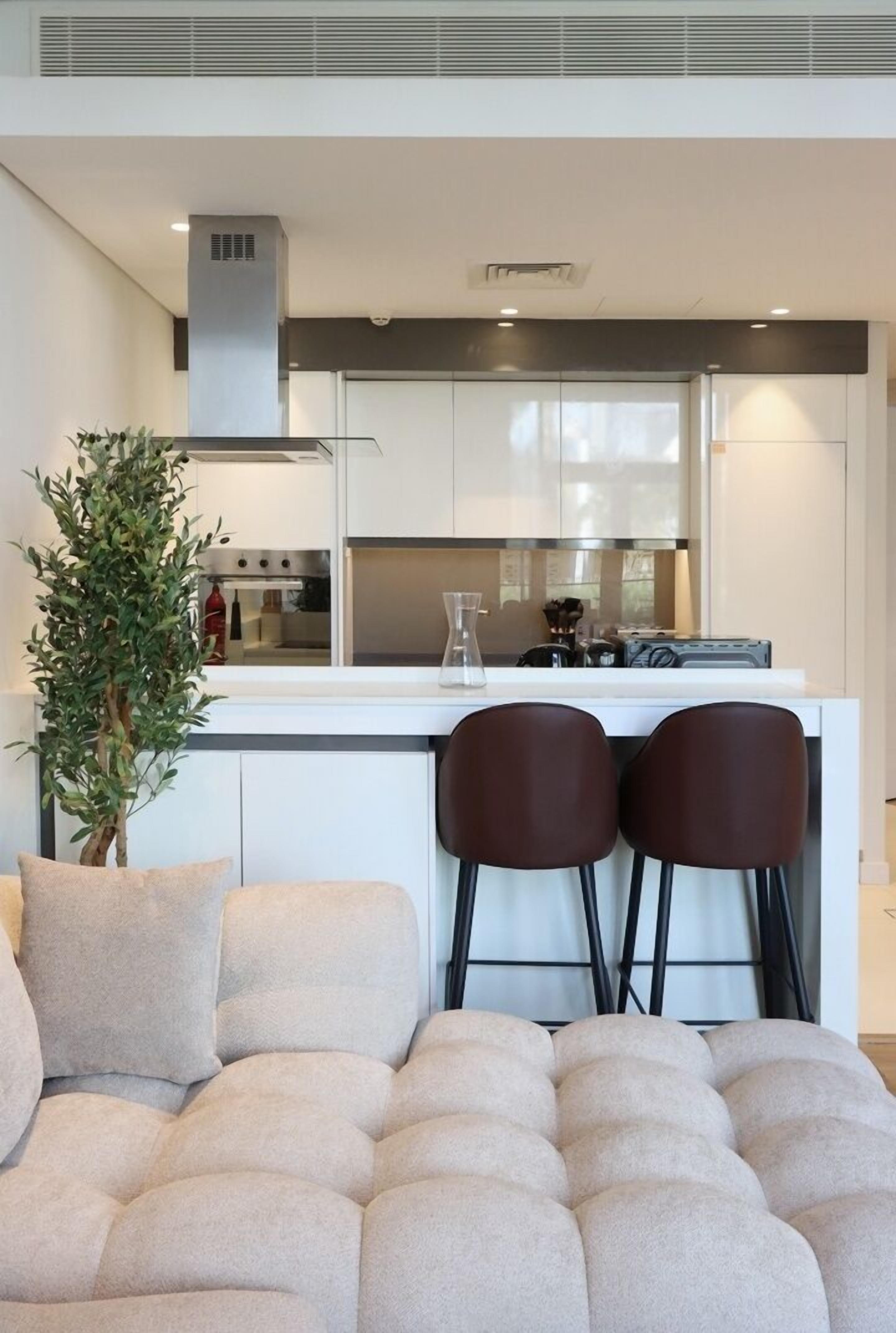 Une cuisine moderne avec des armoires blanches, une hotte de cuisinière en acier inoxydable et un coin bar équipé de deux tabourets.