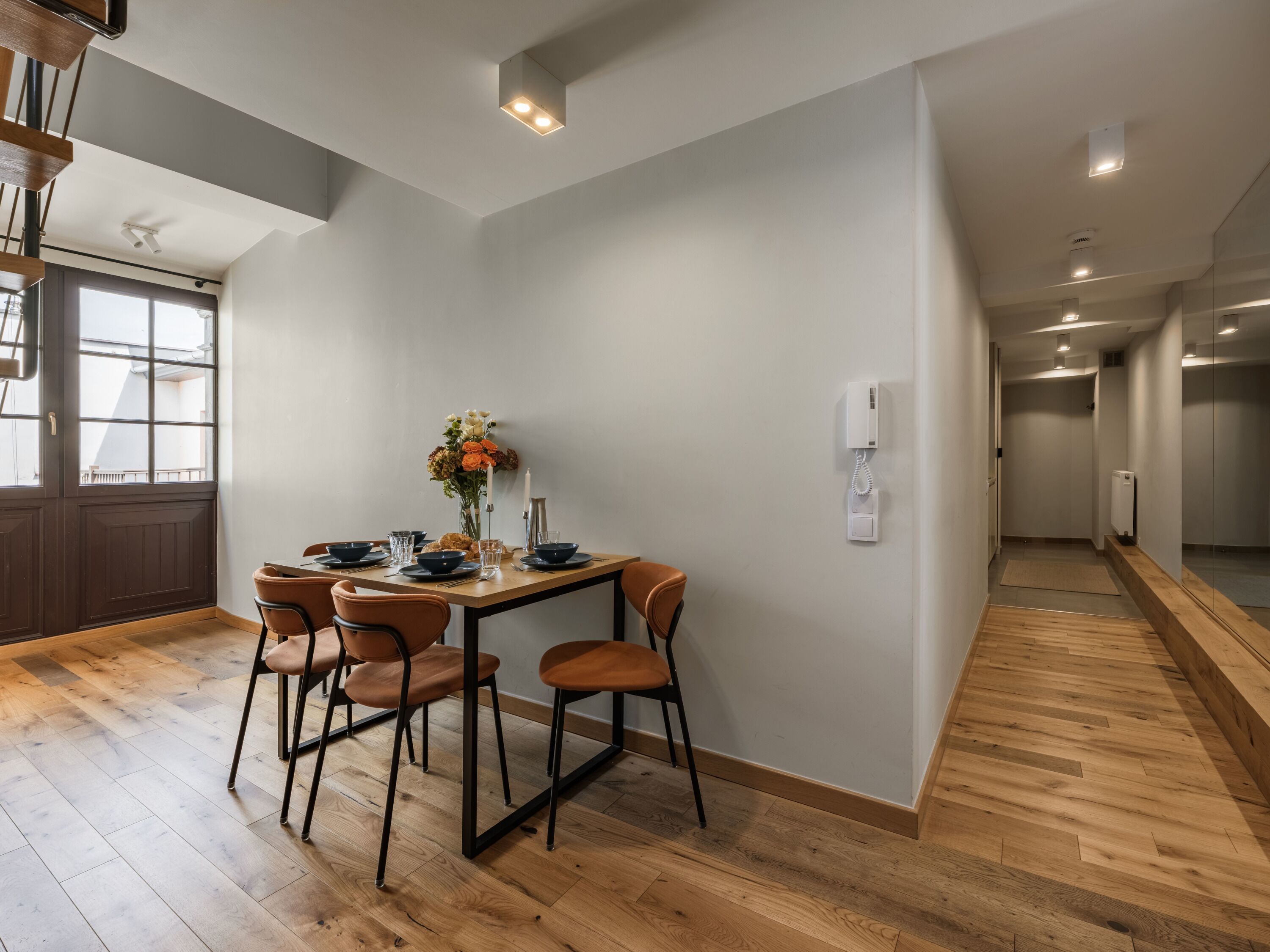 A dining area with a table set for four, wooden flooring, and a view of the adjacent room.