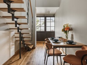 A dining area with a wooden staircase, a table set for four, and a view of the outdoors through a window.
