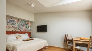 A bedroom with a bed, a wooden desk, and a chair. There's a wall with graffiti art and a flat-screen TV mounted on the wall. - A two-level family apartment (Kraków - Kazimierz & Podgórze)
