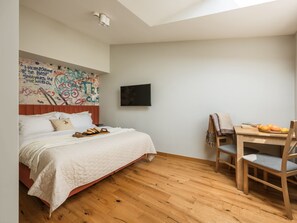 A bedroom with a bed, a wooden desk, and a chair. There's a wall with graffiti art and a flat-screen TV mounted on the wall. - A two-level family apartment (Kraków - Kazimierz & Podgórze)