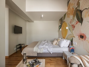 Un dormitorio con cama, mesita de noche, televisor montado en la pared y un mural floral.