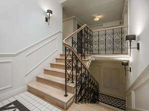 A staircase with a wooden handrail and black wrought iron balusters, white walls, and a patterned floor. - Studio standard for two. (Kraków - Kazimierz & Podgórze)
