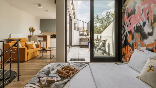 Un dormitori modern amb llit, sofà, zona de menjador i un balcó amb vistes.
