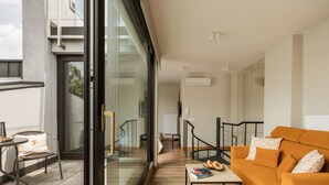 Ein modernes Wohnzimmer mit Glastür zum Balkon, einer Couch, einem Couchtisch und einem kleinen Tisch mit Büchern und Gebäck.