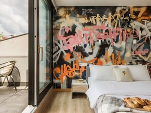 A modern bedroom with a graffiti wall, a bed with pillows, a nightstand, and a window overlooking a building. - Graffiti Studio with Terrace (Kraków - Kazimierz & Podgórze)