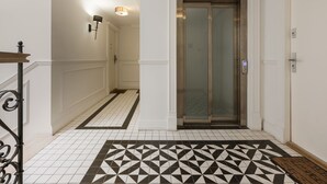 Un passadís amb un paviment estampat, una porta amb panell de vidre i un llum penjant a la paret.