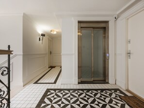 A hallway with a patterned floor, a door with a glass panel, and a wall-mounted light fixture. - Graffiti Studio with Terrace (Kraków - Kazimierz & Podgórze)