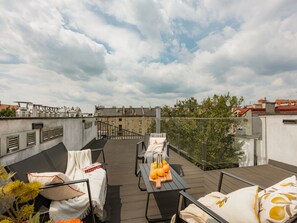 Una terraza en la azotea con mobiliario exterior, una mesa con naranjas y vistas a edificios al fondo.