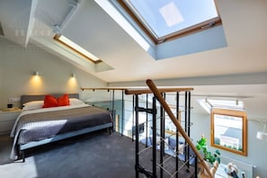 Un dormitorio con tragaluz, cama, escritorio y silla.