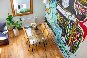 A modern room with a glass table, wooden chairs, a potted plant, and a colorful graffiti wall.