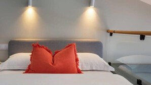 A bed with white bedding and a red pillow, two wall-mounted lights, and a wooden headboard.