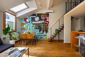 Ein Loft-Wohnraum mit schrägemaßter Decke, Wandgemälde, Essbereich und Treppe.