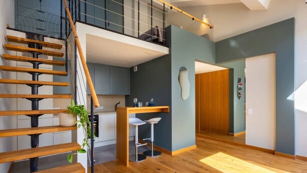 A modern apartment with a wooden staircase, a kitchen with a dining area, and a large window.