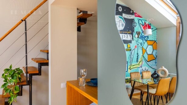 A staircase with wooden steps and metal railings, a dining area with a table and chairs, and a colorful wall with abstract designs. - Studio with a mezzanine (Kraków - Kazimierz & Podgórze)