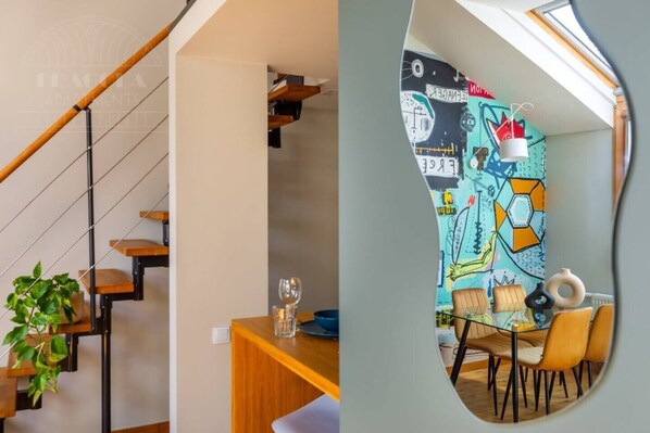 A staircase with wooden steps and metal railings, a dining area with a table and chairs, and a colorful wall with abstract designs.