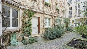 Un stretto sentiero lastricato conduce a un edificio con una porta bianca e finestre, circondato da vegetazione e viti.