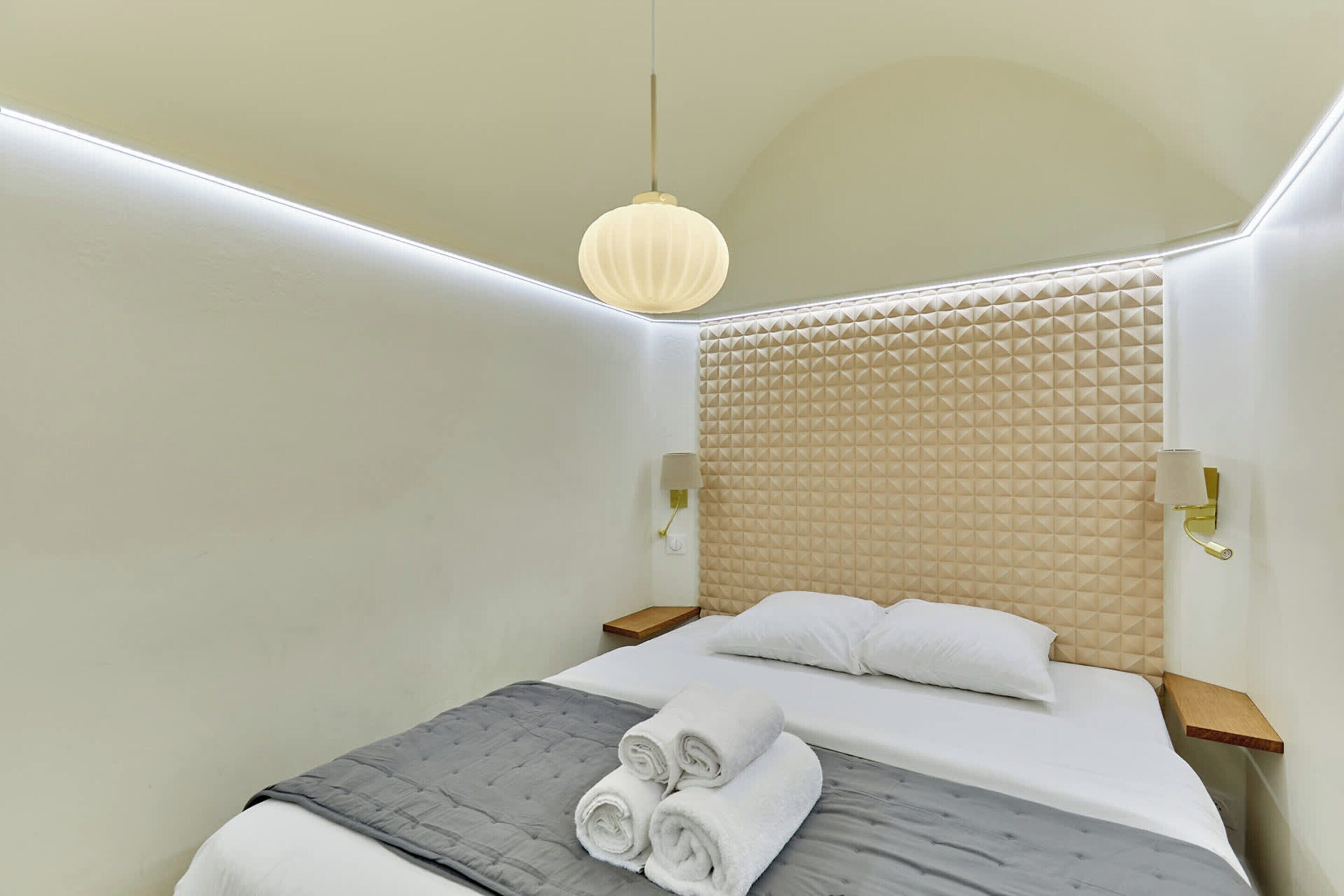 Quarto de hotel moderno com uma cama grande, cabeceira com padrão geométrico e luminária pendente.