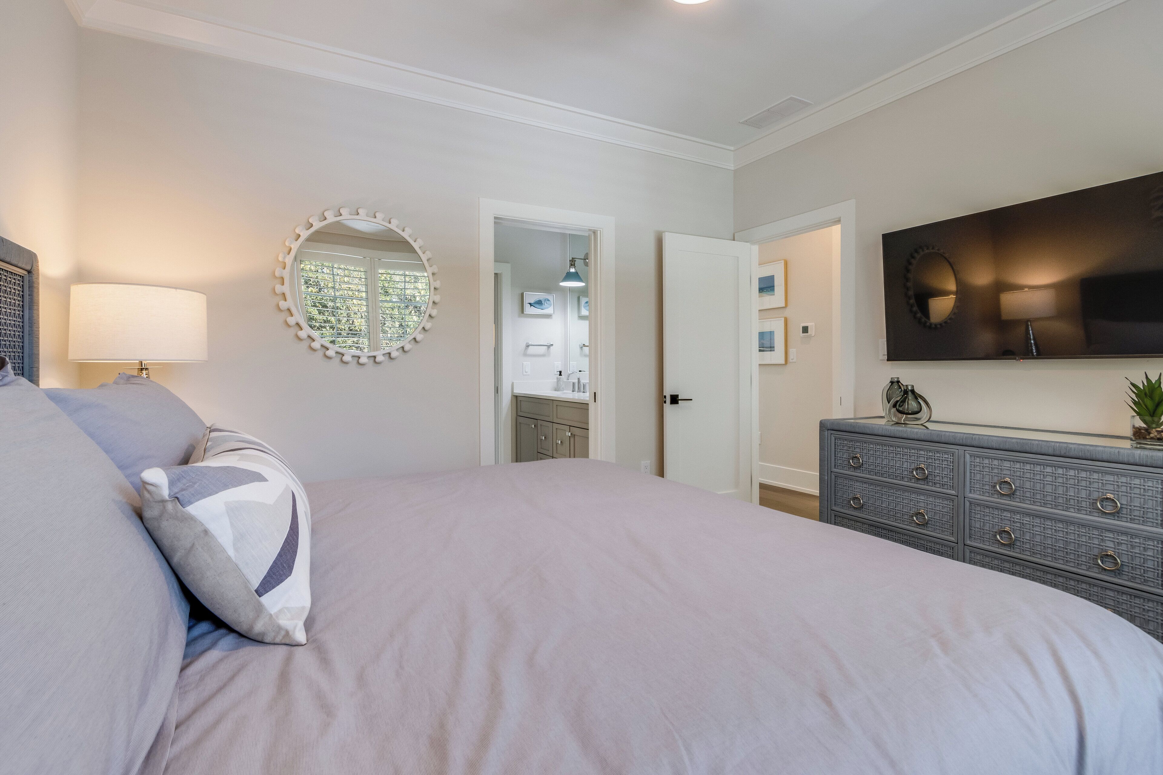 A bedroom with a large bed, a dresser, a mirror, and a television on the wall.
