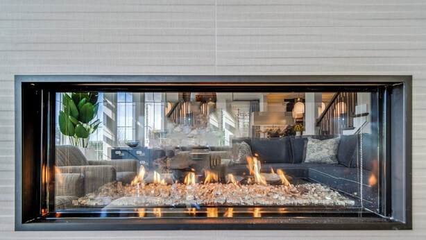 Ein modernes Wohnzimmer mit Kamin mit Glasfront, einem Sofa und einer Treppe, die in einen oberen Bereich führt.