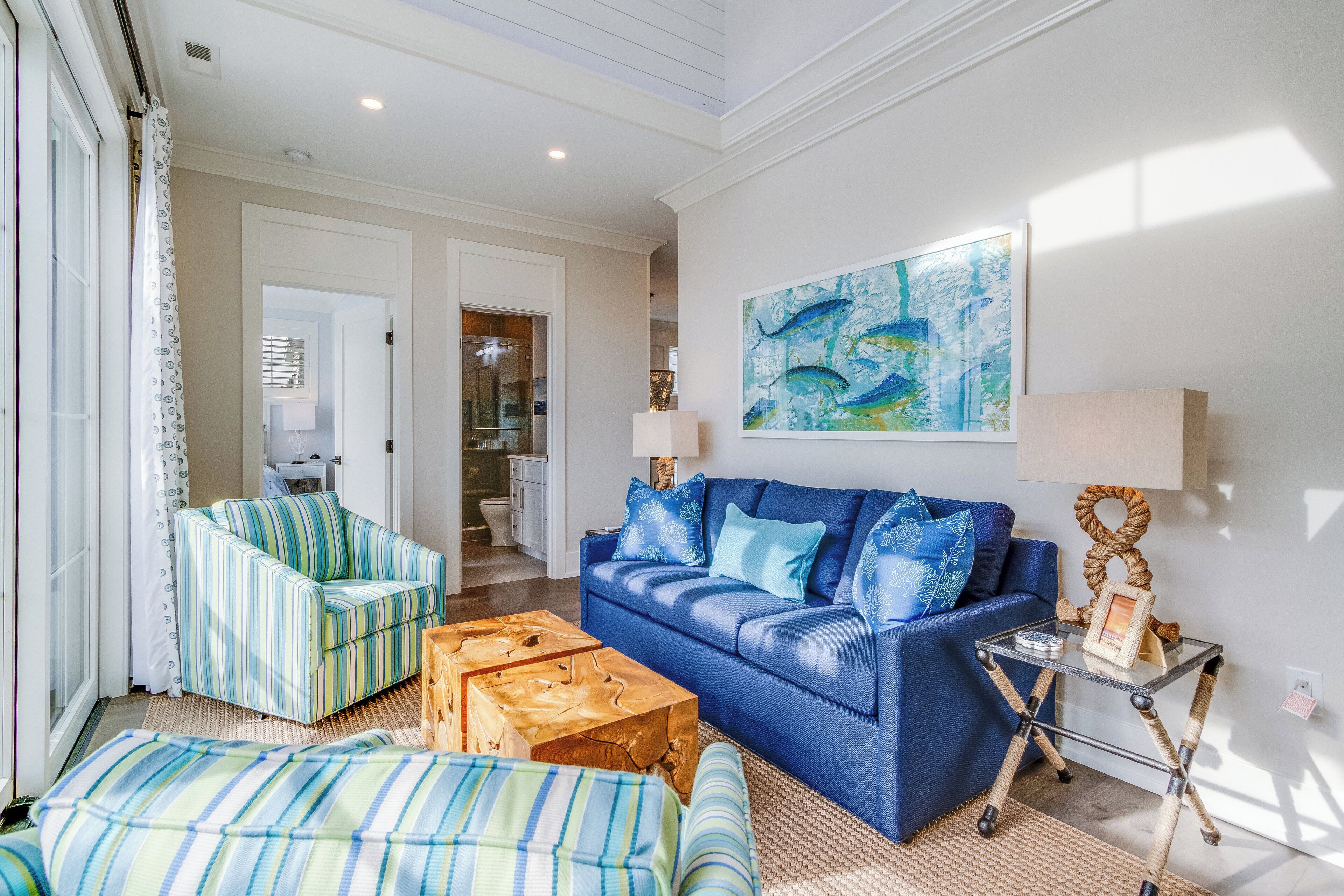 A living room with a blue sofa, striped armchair, and ottoman. There's a glass coffee table and a framed picture on a side table.