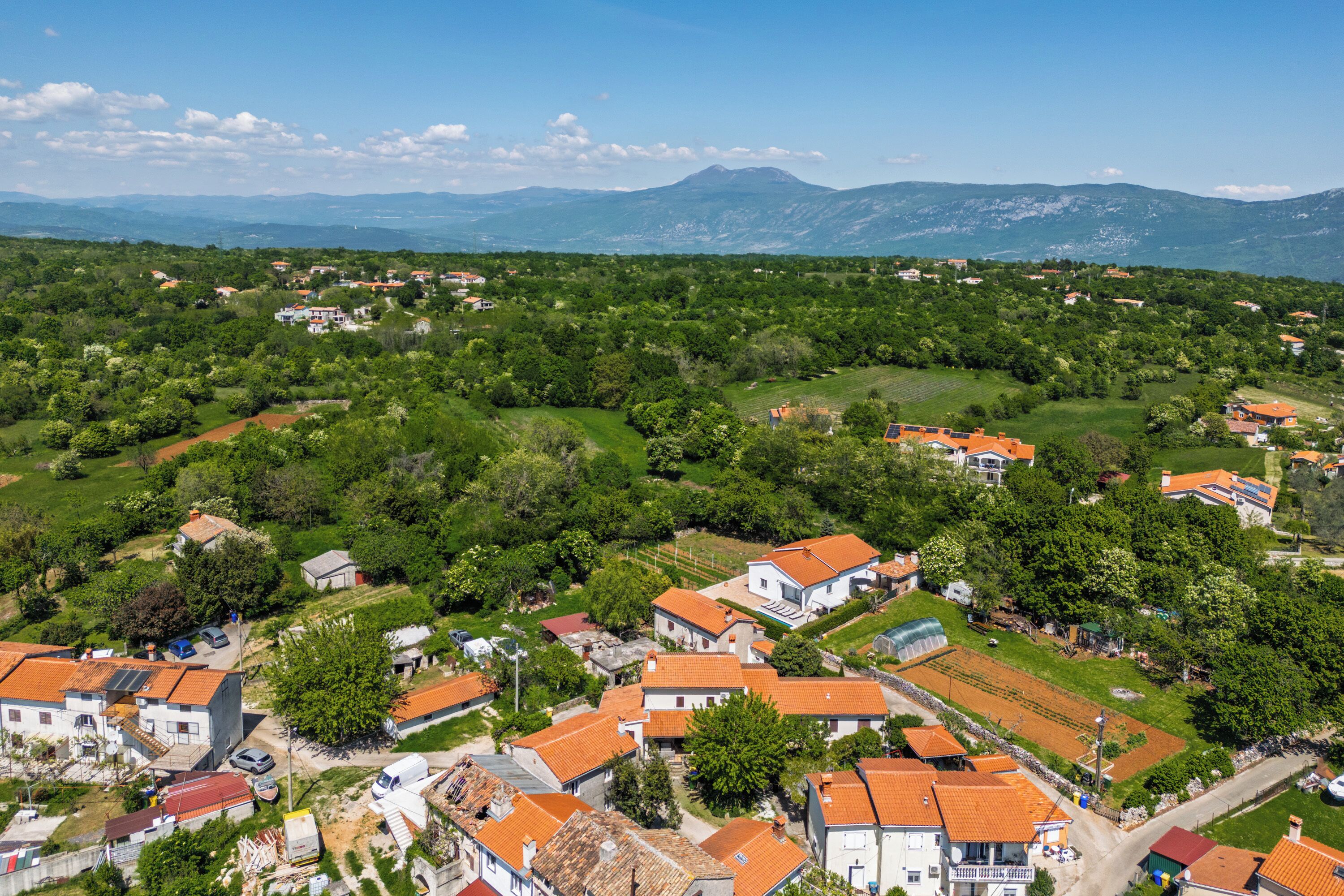 Une vue aérienne d’un village avec des maisons, des champs verdoyants et des montagnes en arrière-plan.