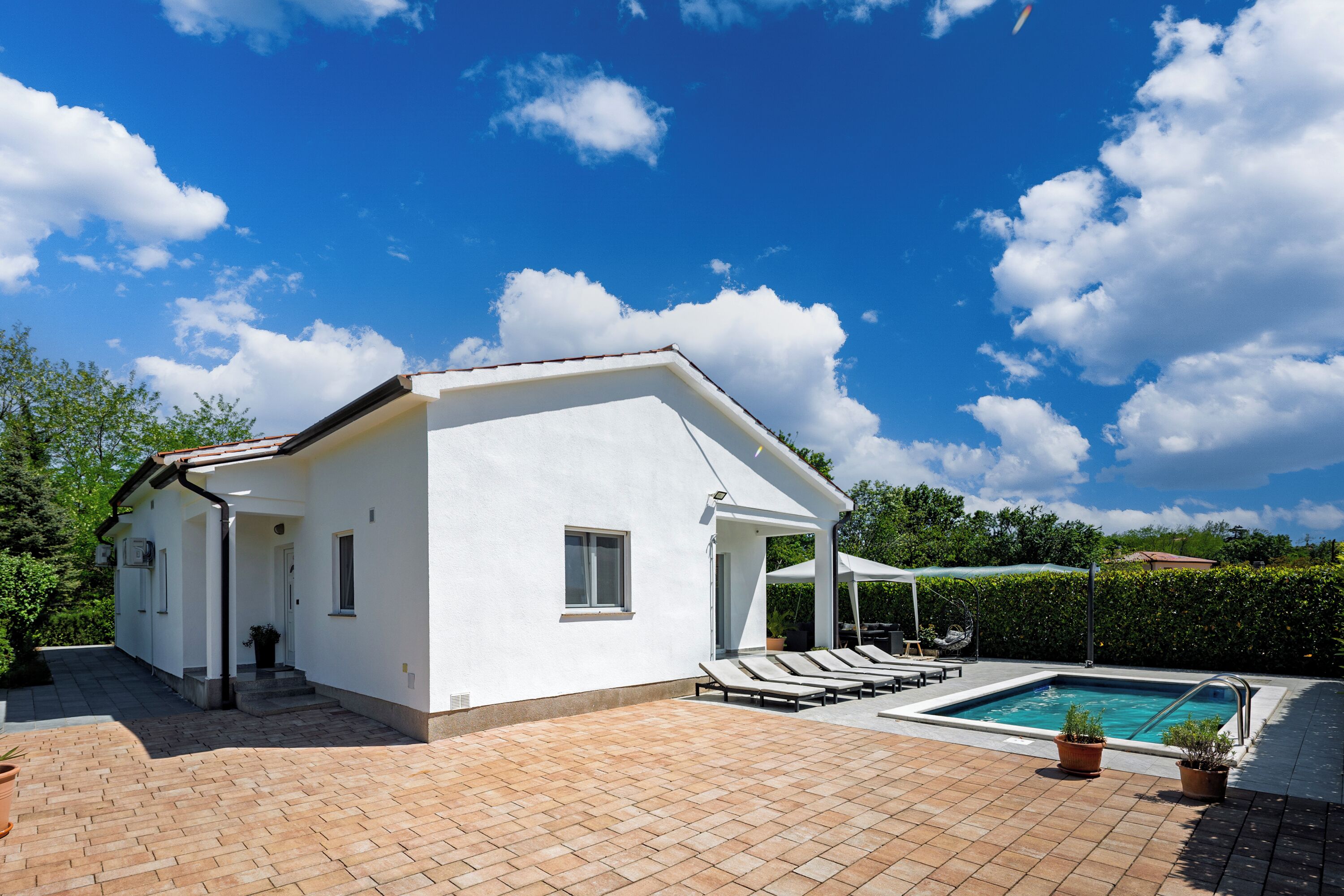 A white building with a swimming pool, lounge chairs, and a covered patio area.