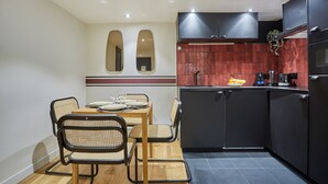 A compact kitchen with a dining area, featuring a modern design with black cabinets, a red backsplash, and a small refrigerator. - Charming Apartment Faubourg St Honore Madeleine (Paris)