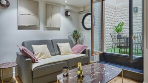 A modern living room with a grey sofa, a marble coffee table, and a view of an outdoor patio with a table and chairs. - Charming Apartment Faubourg St Honore Madeleine (Paris)