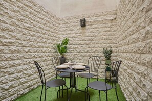 A small, enclosed patio area with a stone wall, a round table set for four, and four chairs. - Charming Apartment Faubourg St Honore Madeleine (Paris)
