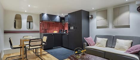 A compact living space with a dining area, kitchenette, and a sofa with cushions.