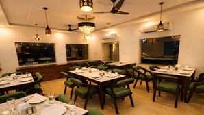A restaurant with multiple tables set for dining, green upholstered chairs, ceiling fans, and pendant lighting. - Aqua Tree Resort (Mohan Chatti)