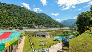 A hotel with a pool, outdoor seating, and a view of the surrounding mountains. - Aqua Tree Resort (Mohan Chatti)