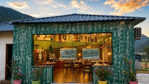 A rustic bar with a wooden interior, large windows, and potted plants. - Aqua Tree Resort (Mohan Chatti)