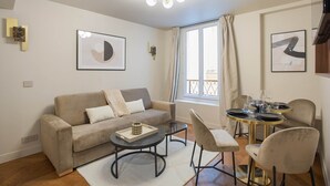 A modern living room with a sofa, coffee table, and dining area with chairs and a table. - New Apartment Center of Paris (Paris)