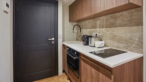 A compact kitchen with a dark door, wooden cabinets, a white countertop, a built-in oven, a coffee maker, and a toaster. - New Apartment Center of Paris (Paris)