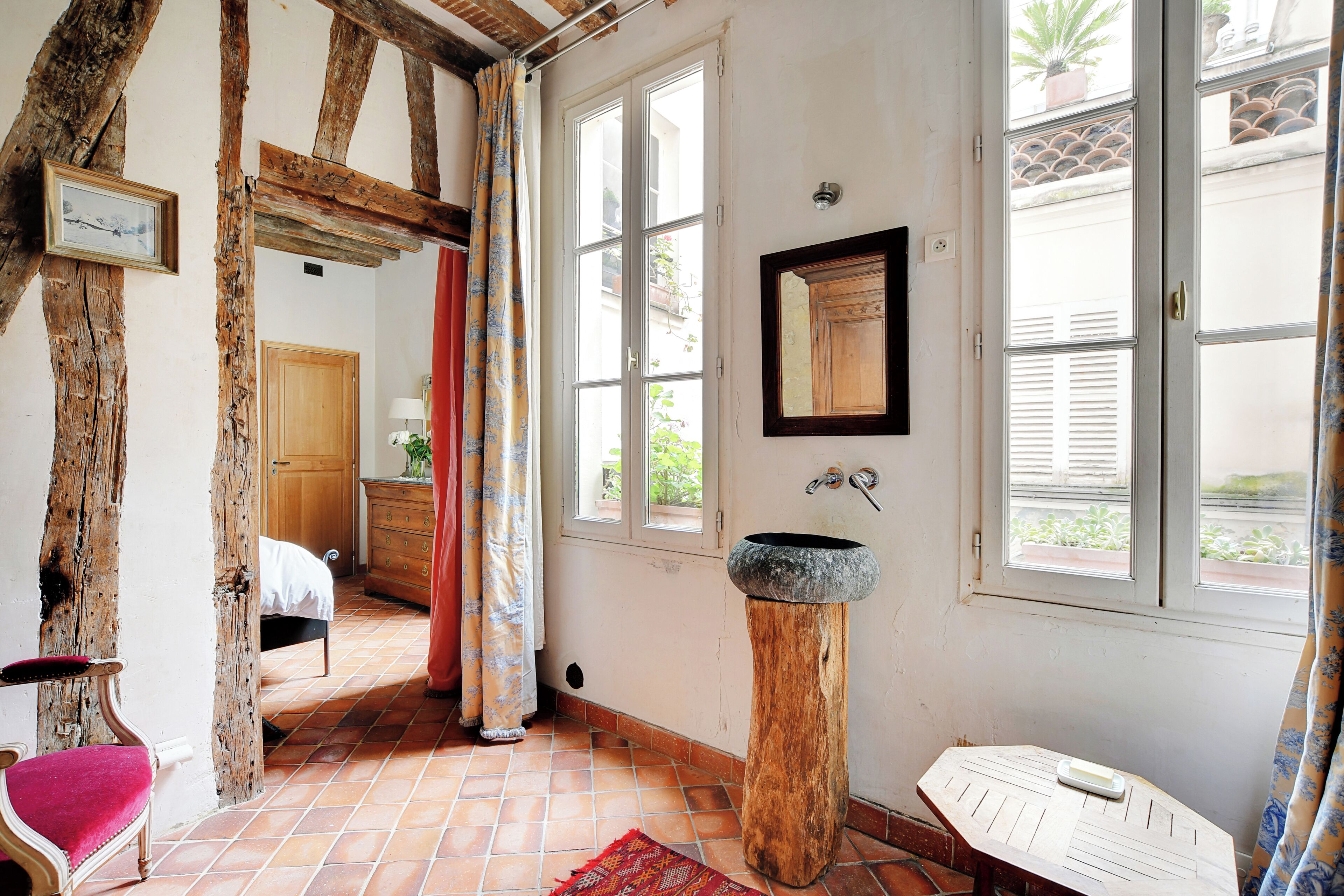 Una habitación rústica con vigas de madera a la vista, una cama, un taburete de madera y un lavabo de piedra.