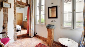A rustic room with exposed wooden beams, a bed, a wooden stool, and a stone sink.