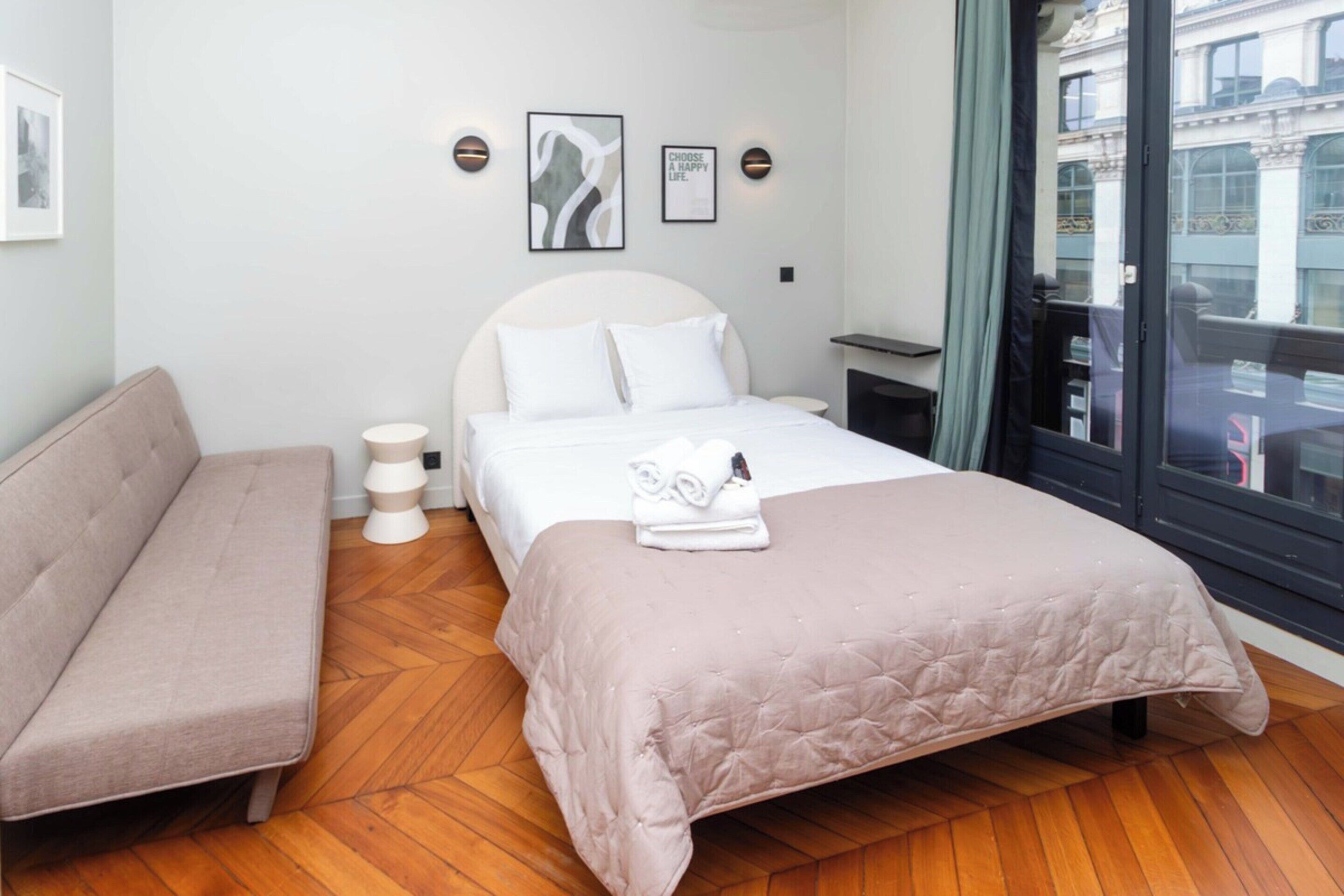 A modern hotel room with a bed, a bench, and a view of the city.