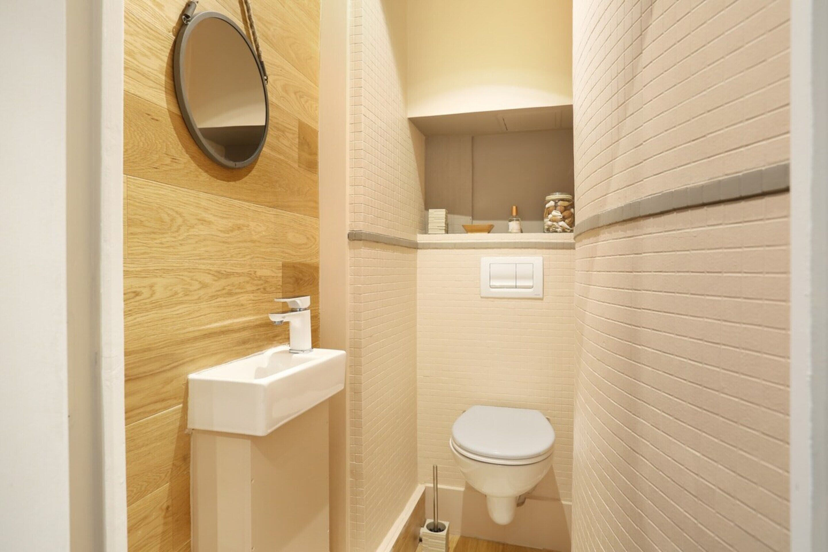 A small bathroom with a wooden vanity, a white sink, a toilet, and a mirror.