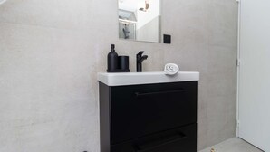 Ein modernes Badezimmer mit einem weißen Waschbecken, einem schwarzen Schrank und einem Spiegel darüber.